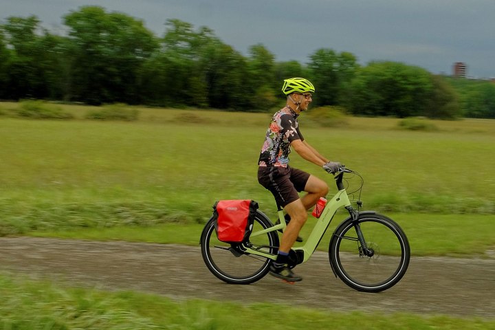 Person in floral shirt cycling on a path in a park.
