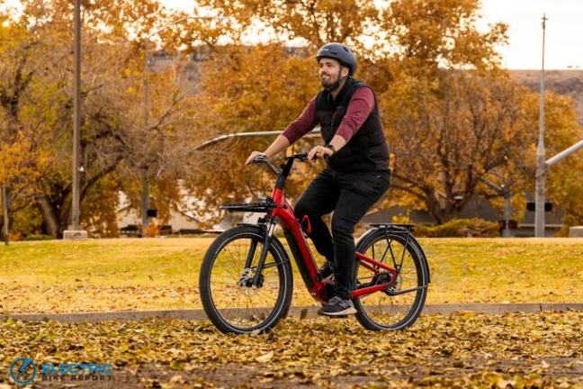 Person riding a red bicycle in a park with autumn leaves on the ground.