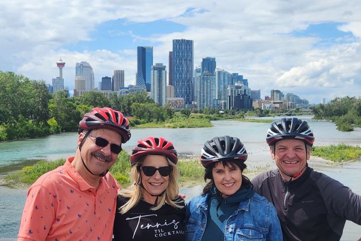 Four people in helmets posing on a bridge with city skyline in the background.