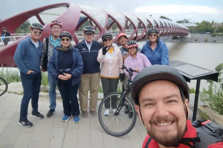 Group of cyclists in helmets smiling in front of a red bridge over a river.