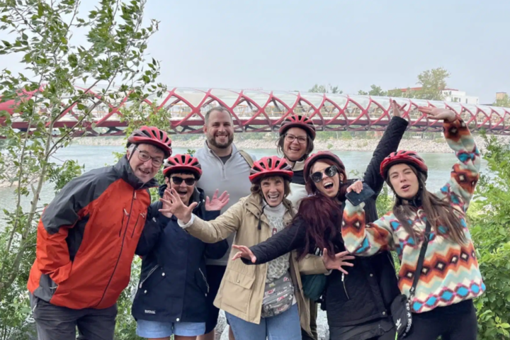 Group of people in bike helmets posing in front of distinctive red bridge over water.