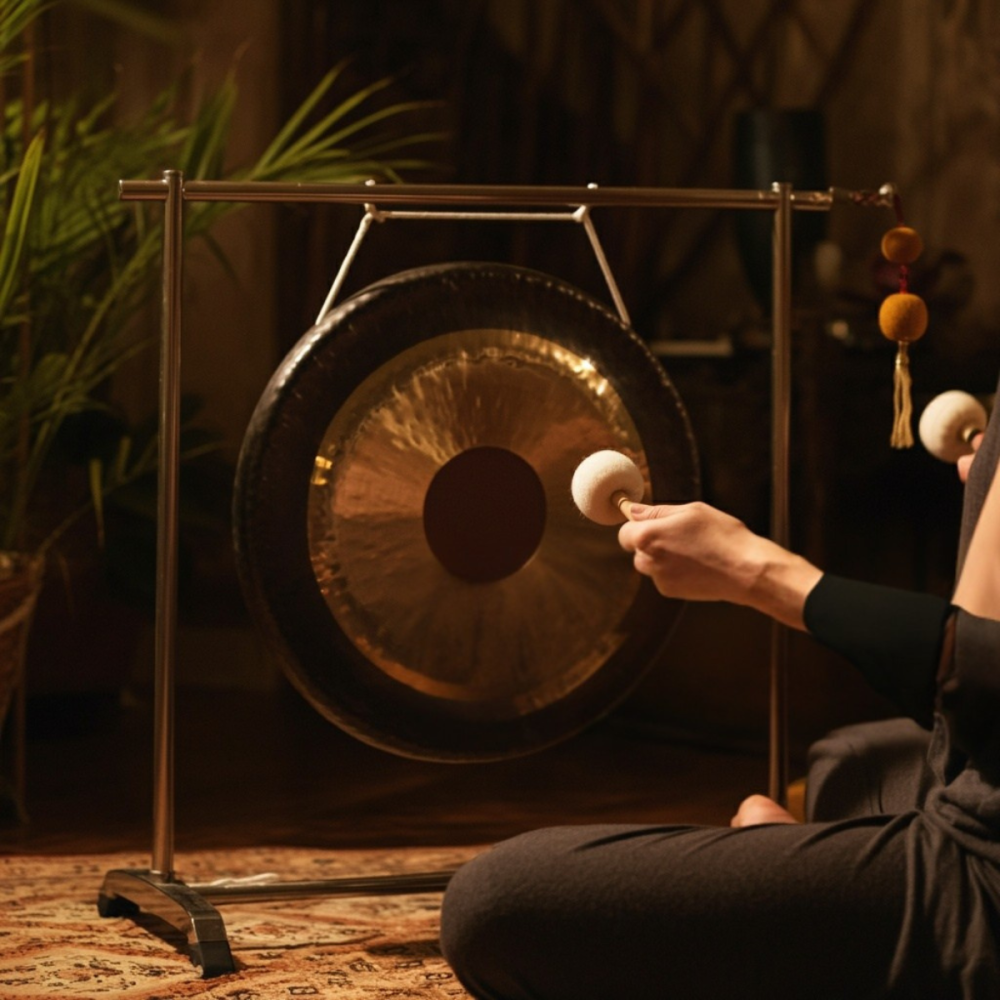 Person striking a large gong in a dimly lit room.
