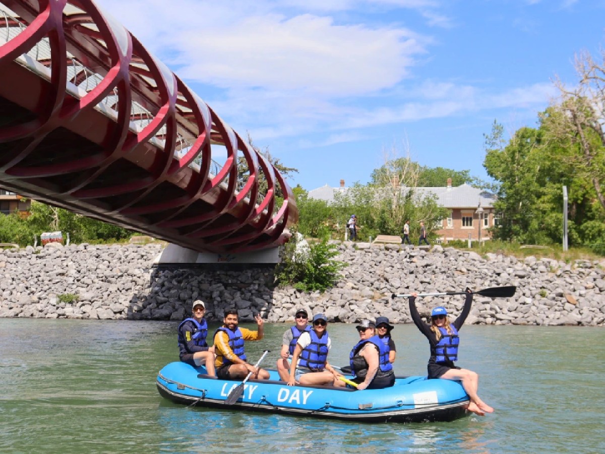 Group rafting under a red bridge on a river, people wearing life vests and helmets.