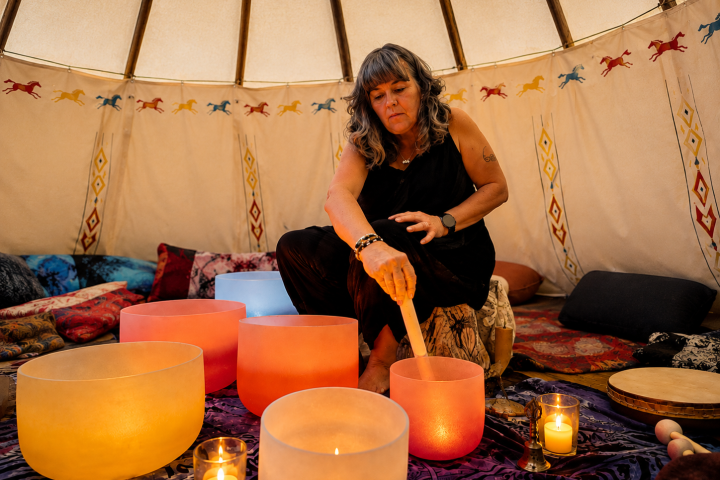 Woman playing crystal bowls in a decorated tent with candles.