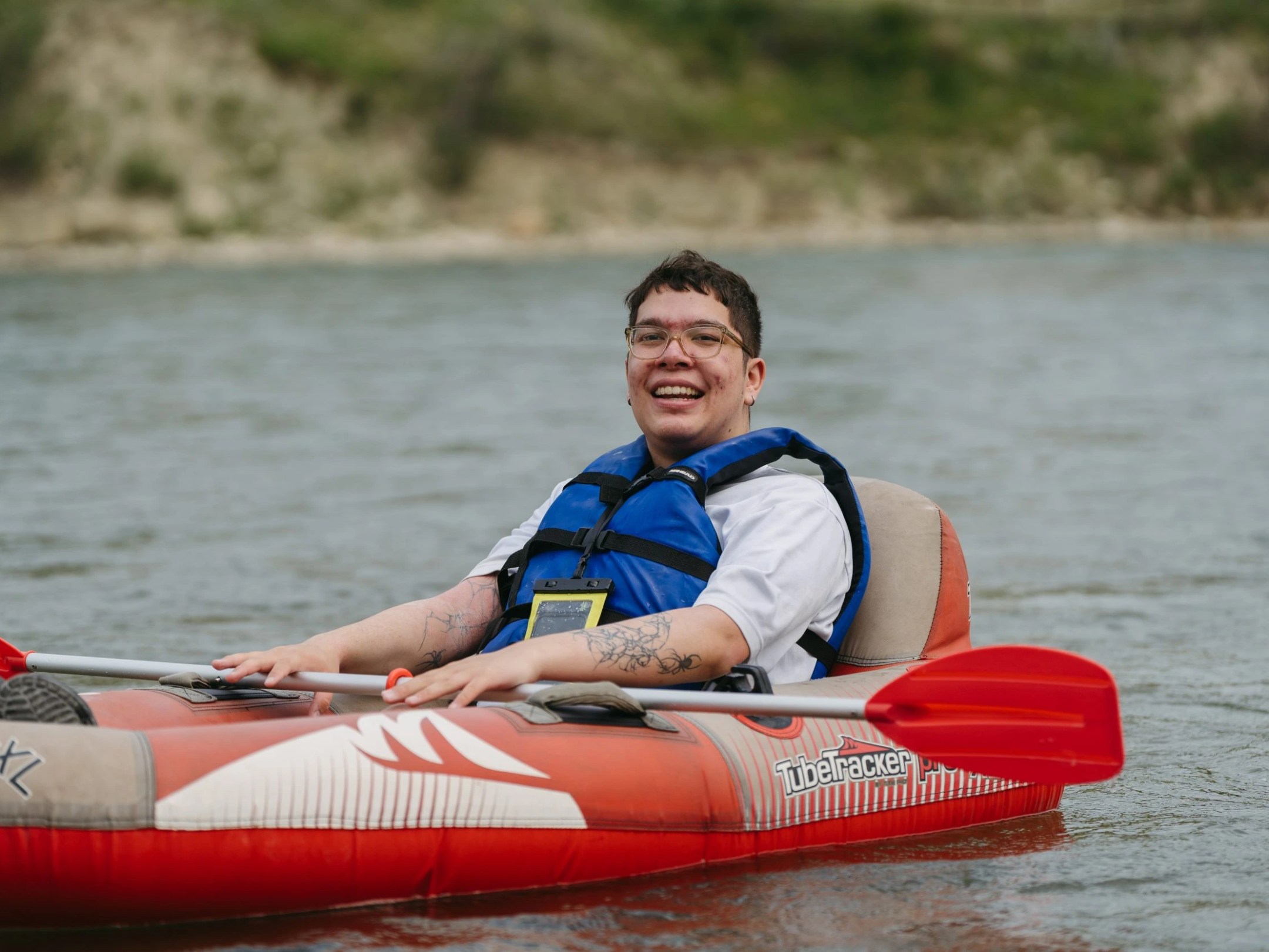 Person smiling in a red inflatable kayak on a river.