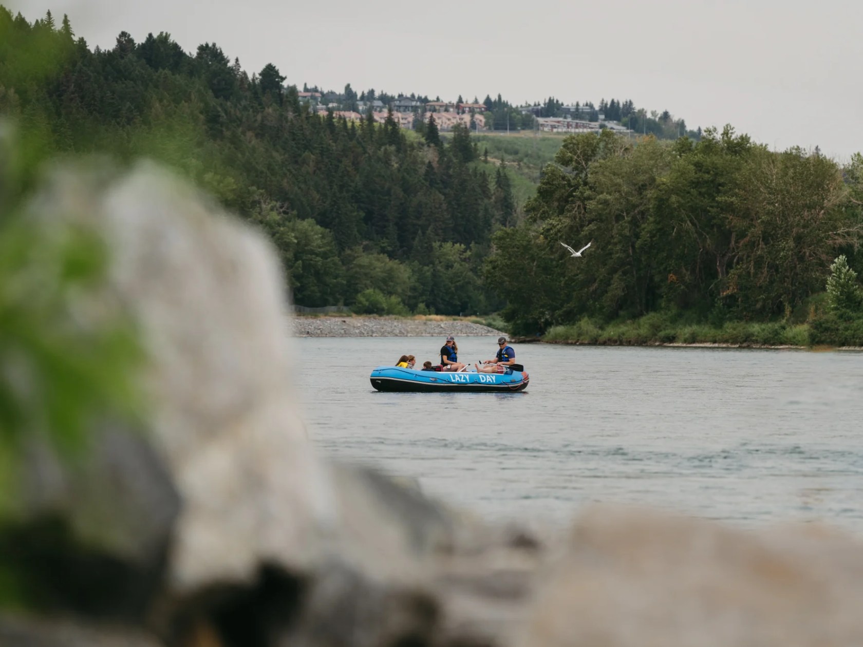 People rafting on a river with trees and buildings in the background.