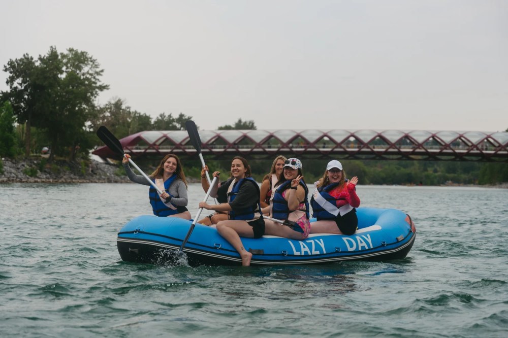 Group of women paddling on a blue raft in a river.