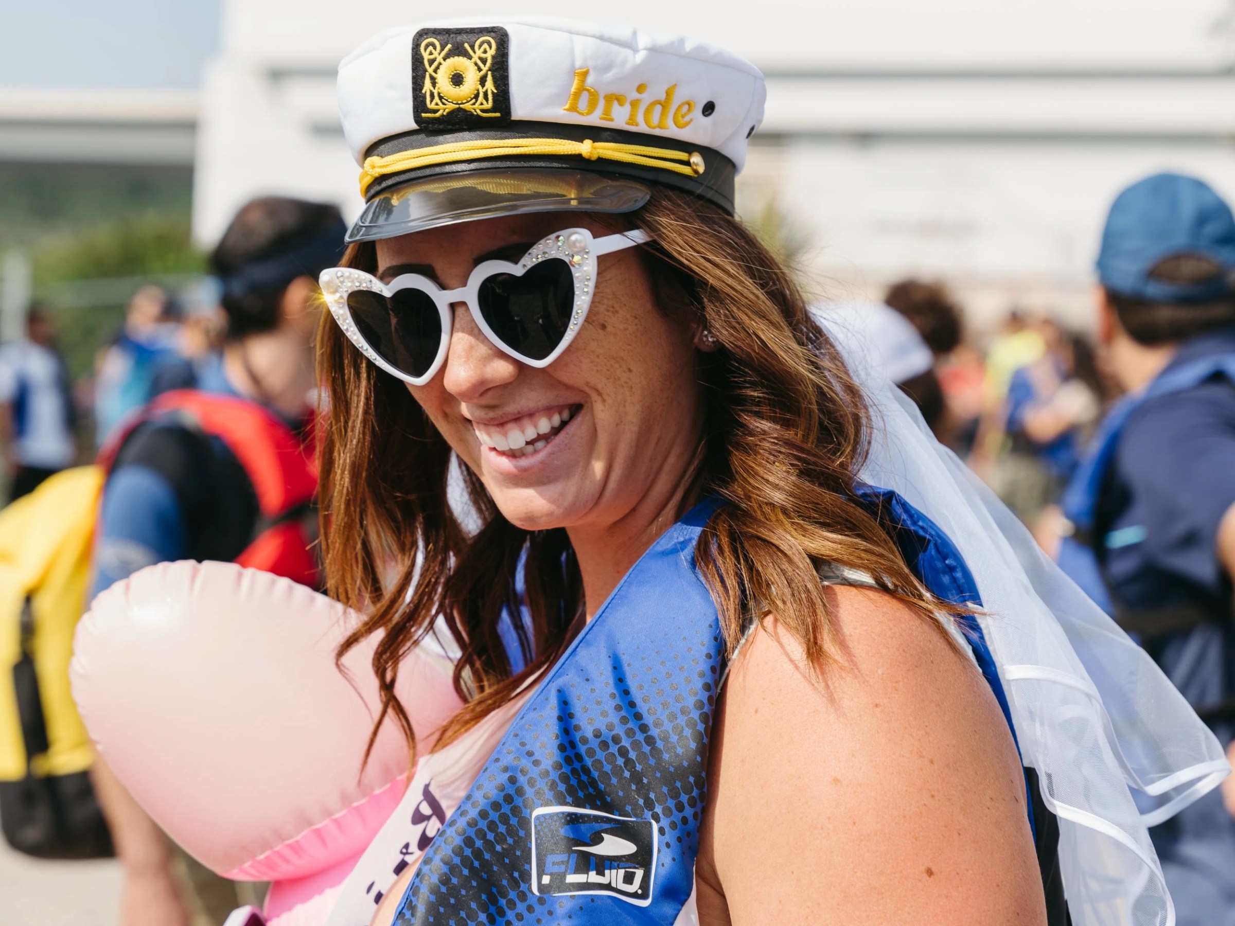 Smiling woman in captain hat and heart sunglasses at outdoor event.