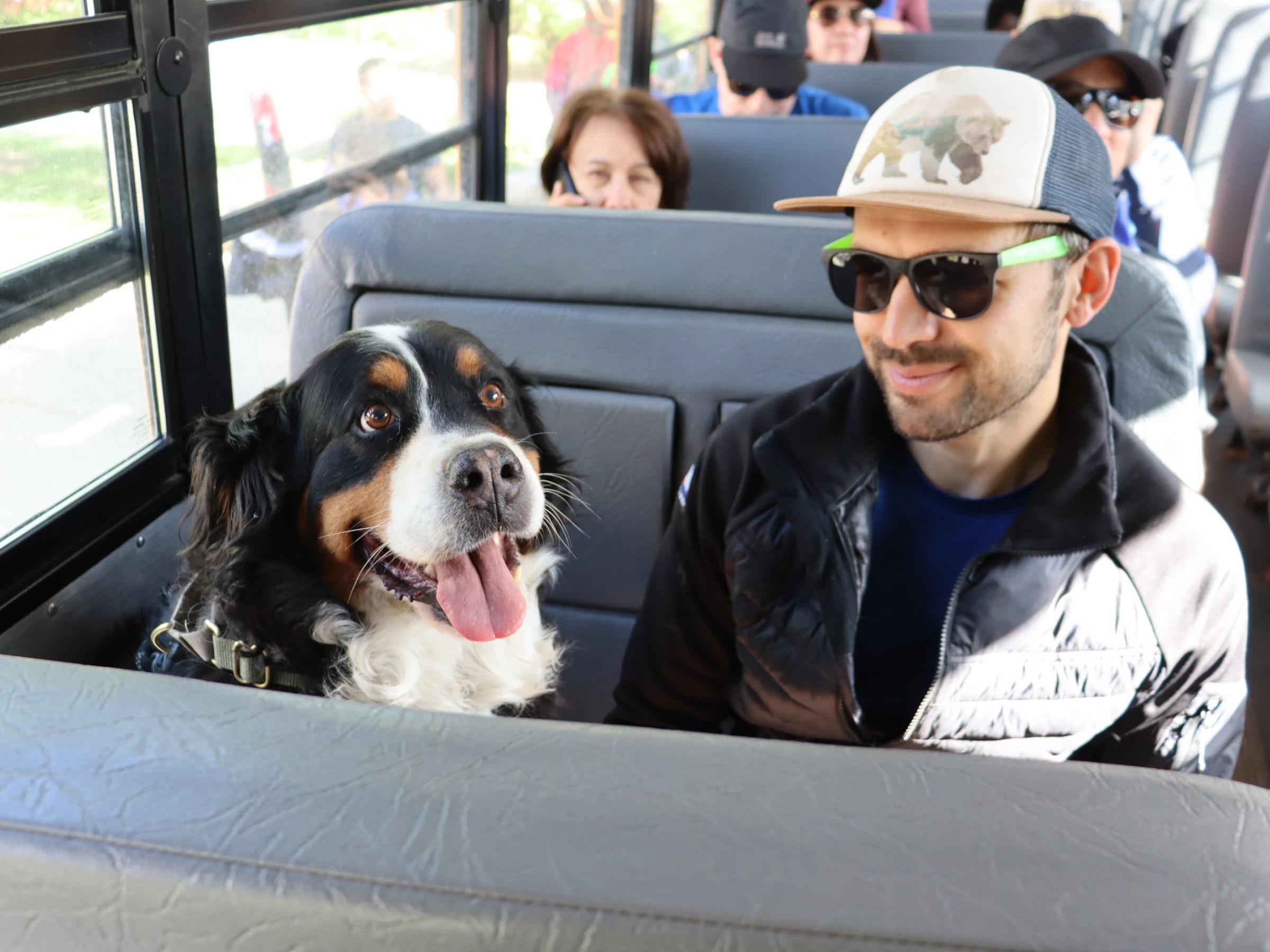 Man in sunglasses with a dog on a bus seat.