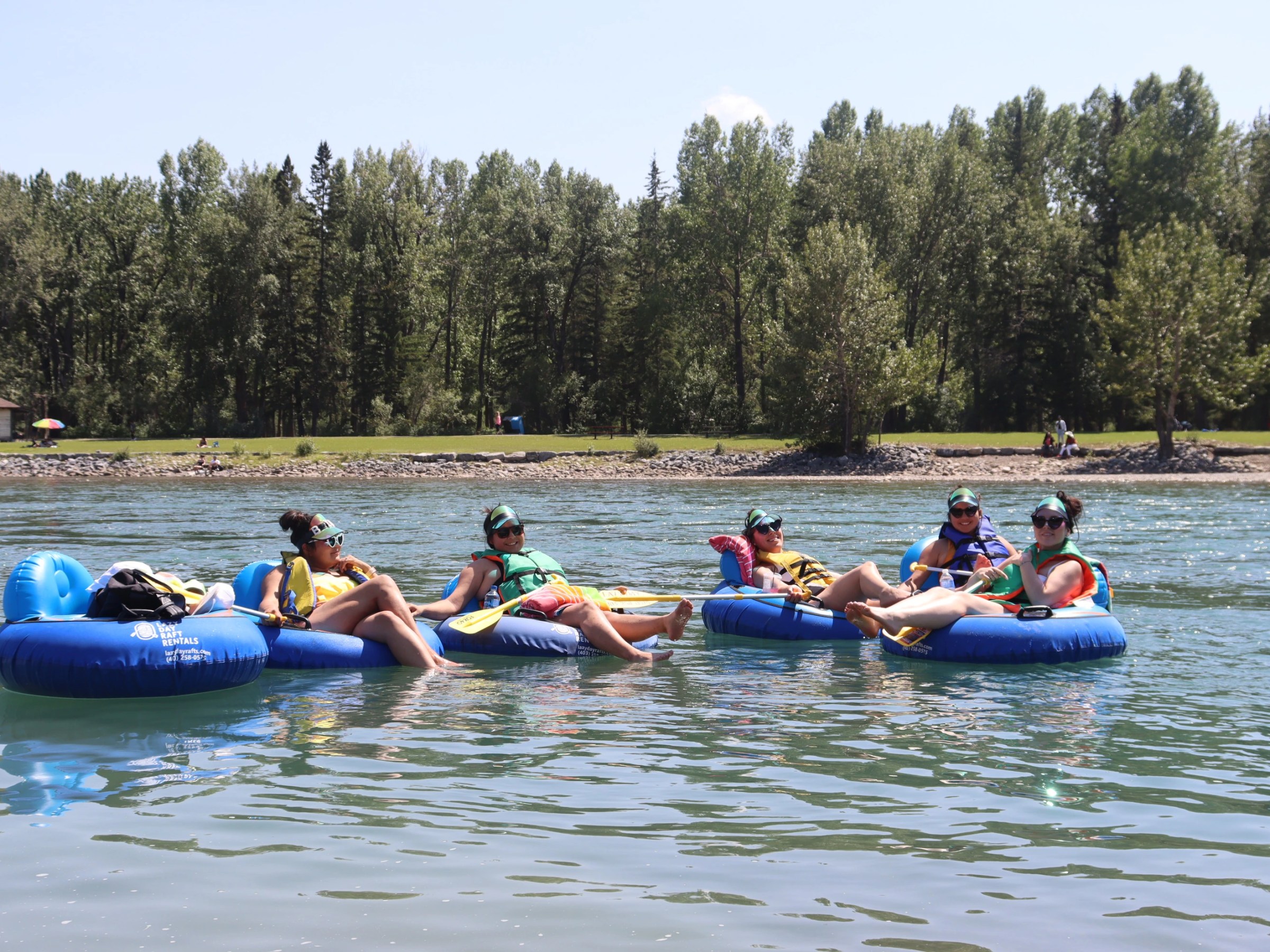 Five people floating on blue tubes in a river with a tree-lined bank.