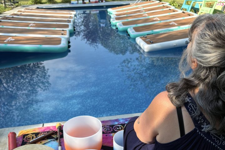 Woman sitting by a pool with musical bowls and drums on a sunny day.