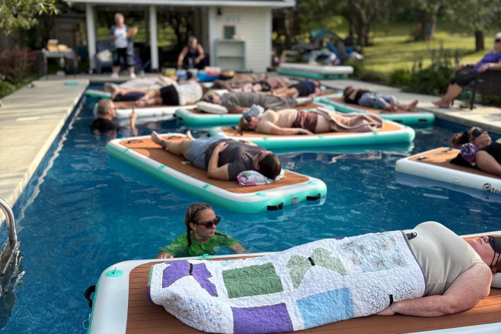 People lying on paddle boards in a pool under a clear sky.