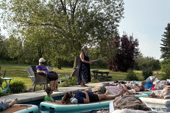 People relaxing on floating tubes in a pool surrounded by trees.