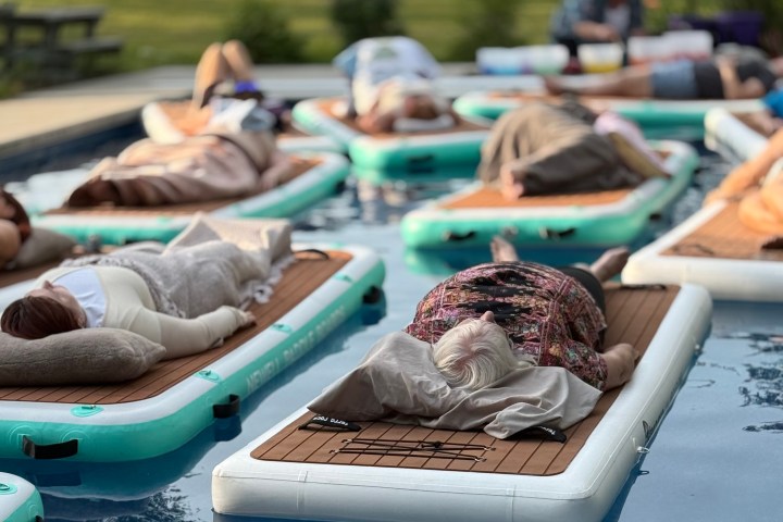 People relaxing on floating mats in a pool with greenery in the background.
