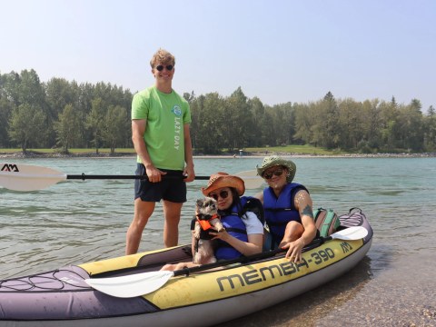 Three people and a dog in a kayak by the river.