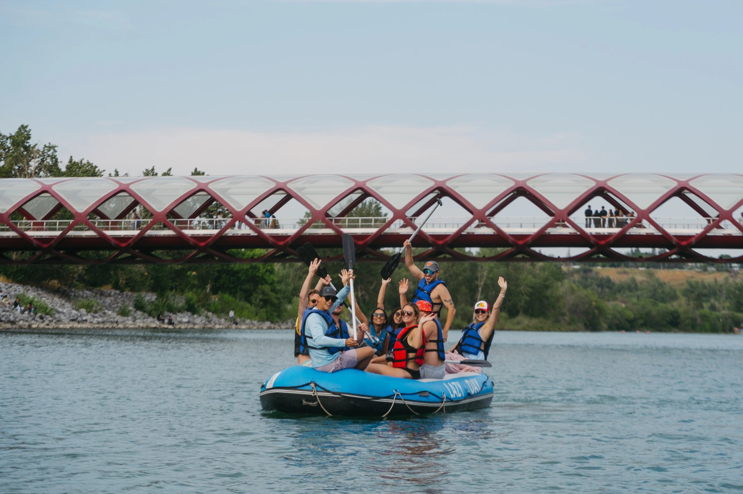 Group rafting on a river under a red bridge during daytime.