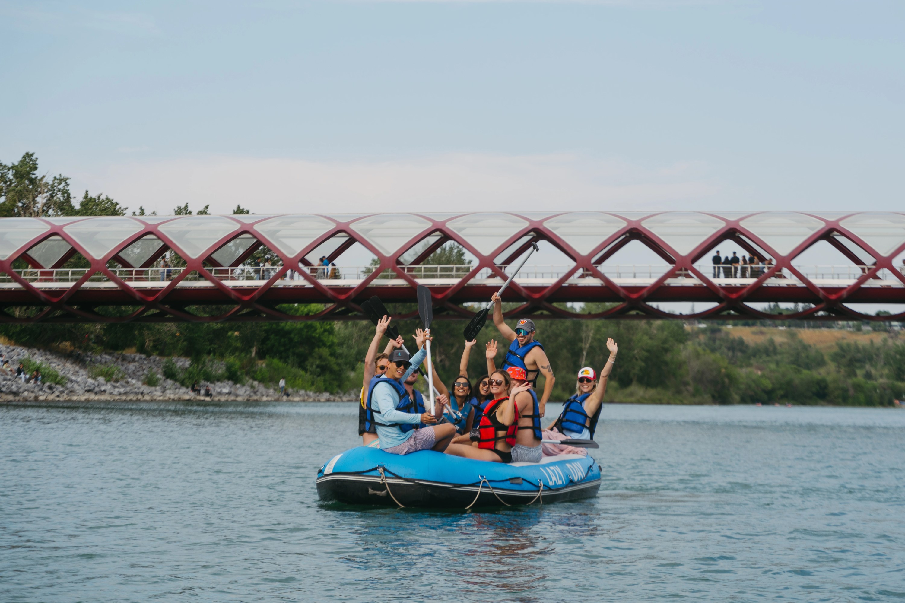 Group rafting on a river under a red bridge during daytime.