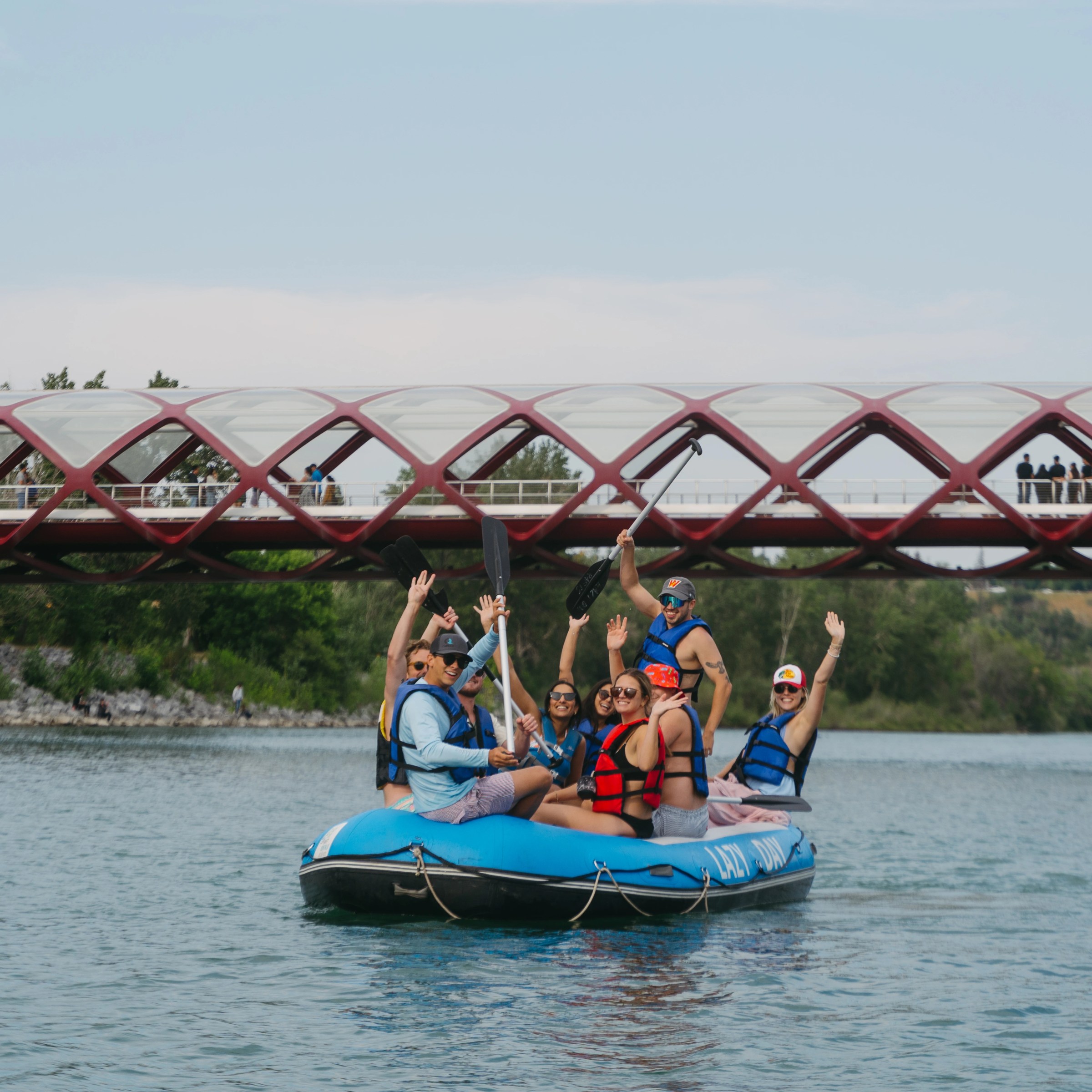 Group rafting on a river under a red bridge during daytime.
