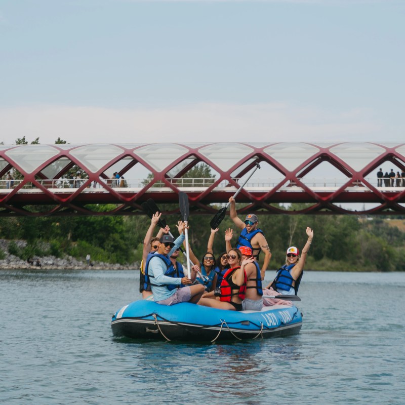 Group rafting on a river under a red bridge during daytime.
