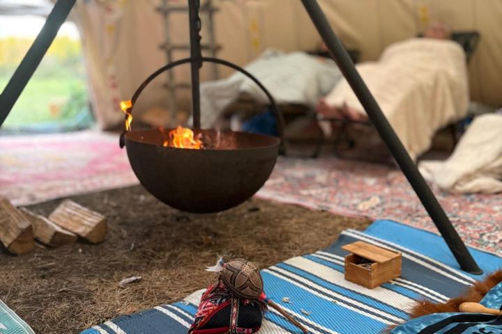 Cozy tent interior with a tripod fire pit, colorful rugs, and bags on the ground.