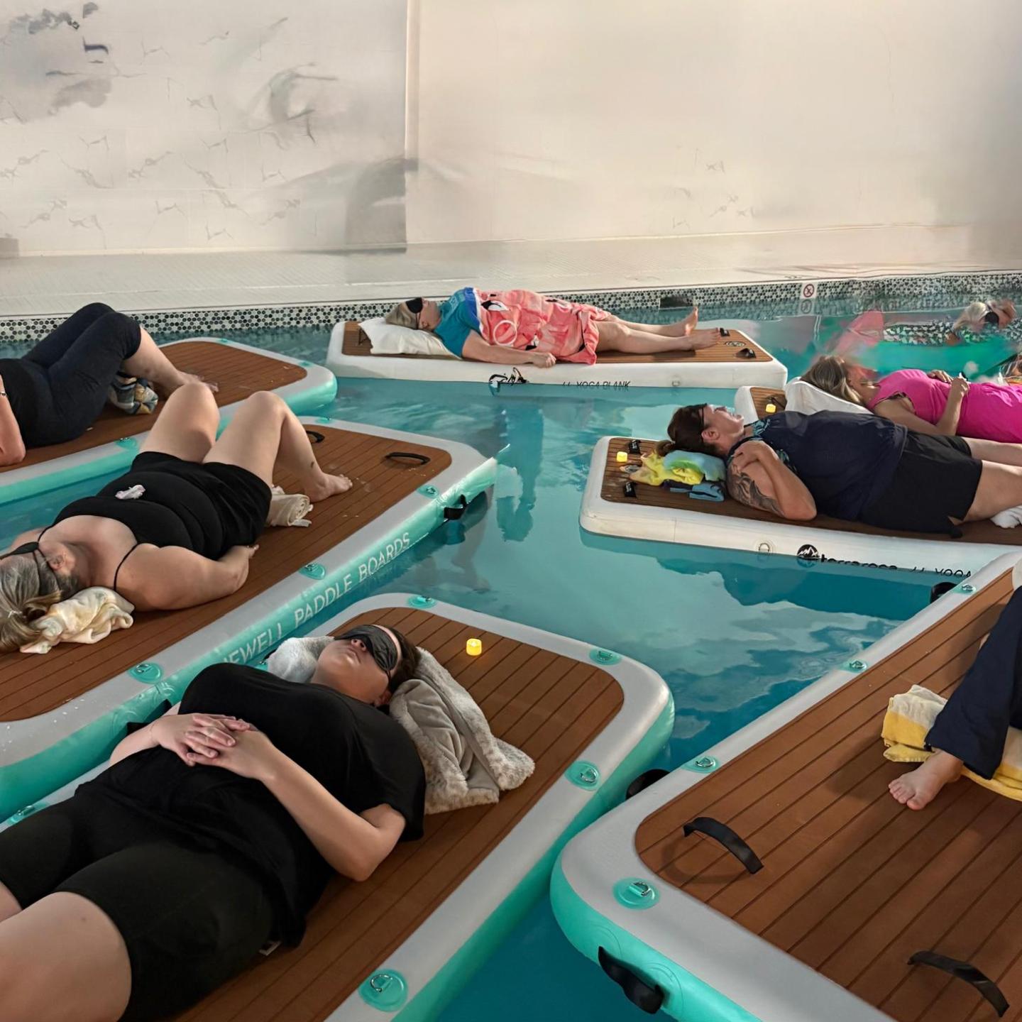 People relaxing on floating mats in an indoor pool.