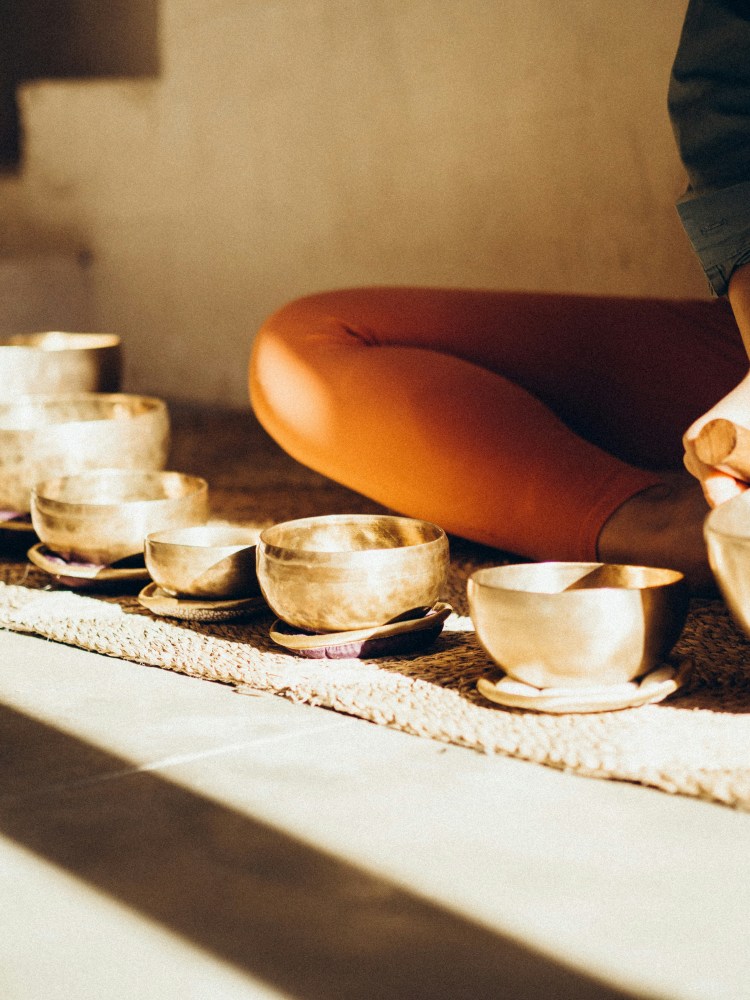 Person seated on floor with seven singing bowls arranged in front.