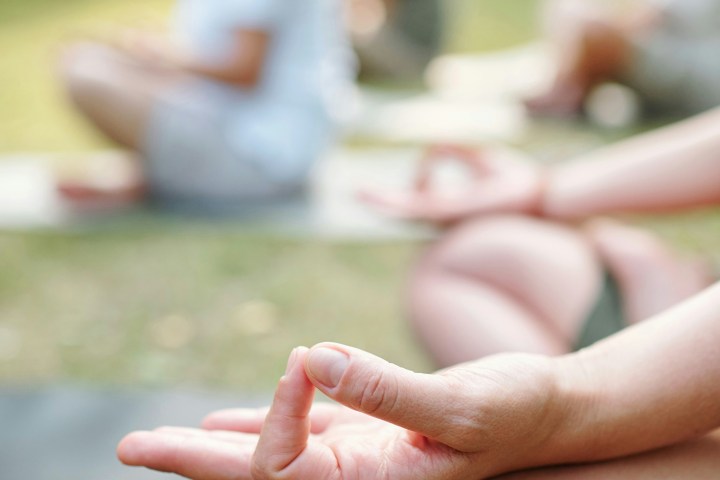 People practicing yoga outdoors, focus on hand in meditation pose.