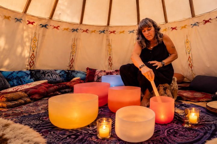Woman playing singing bowls in a decorated tent with candles.