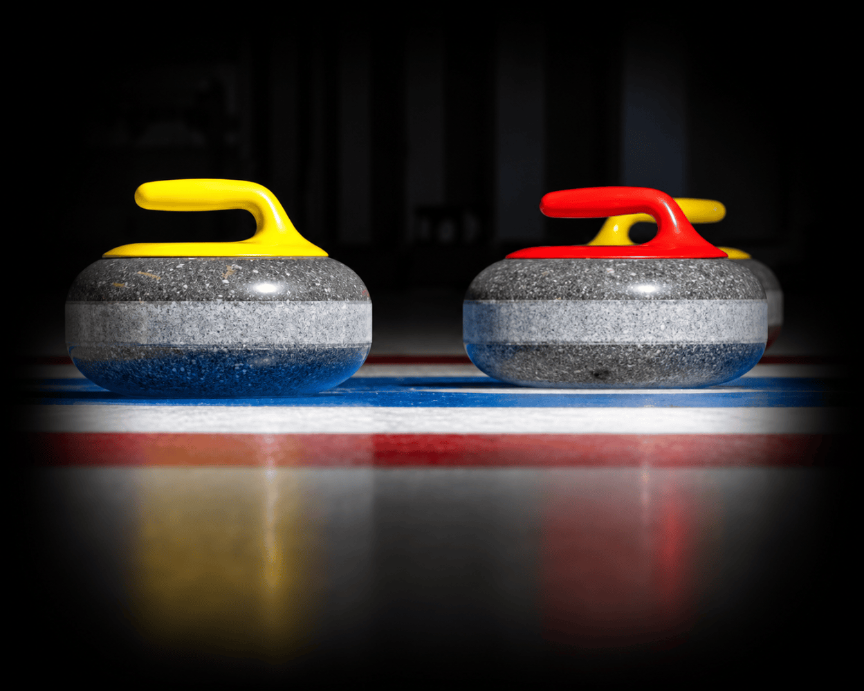 Two curling stones with yellow and red handles on ice.