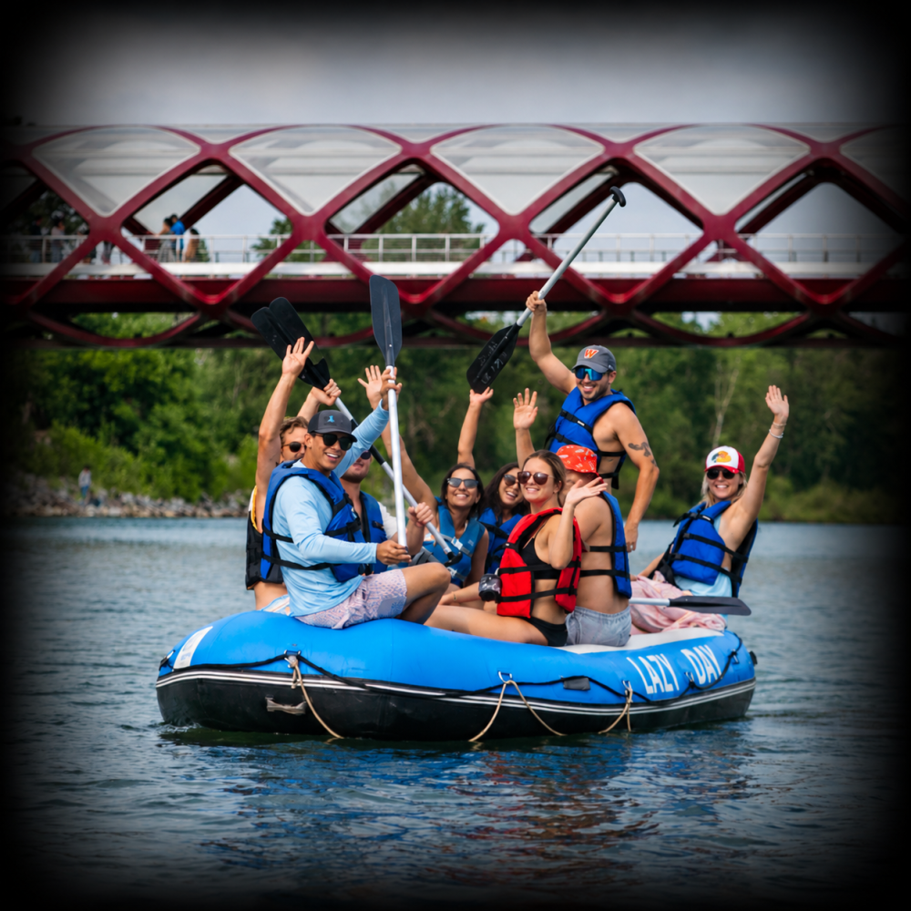 Group of people in a raft waving under a red bridge.