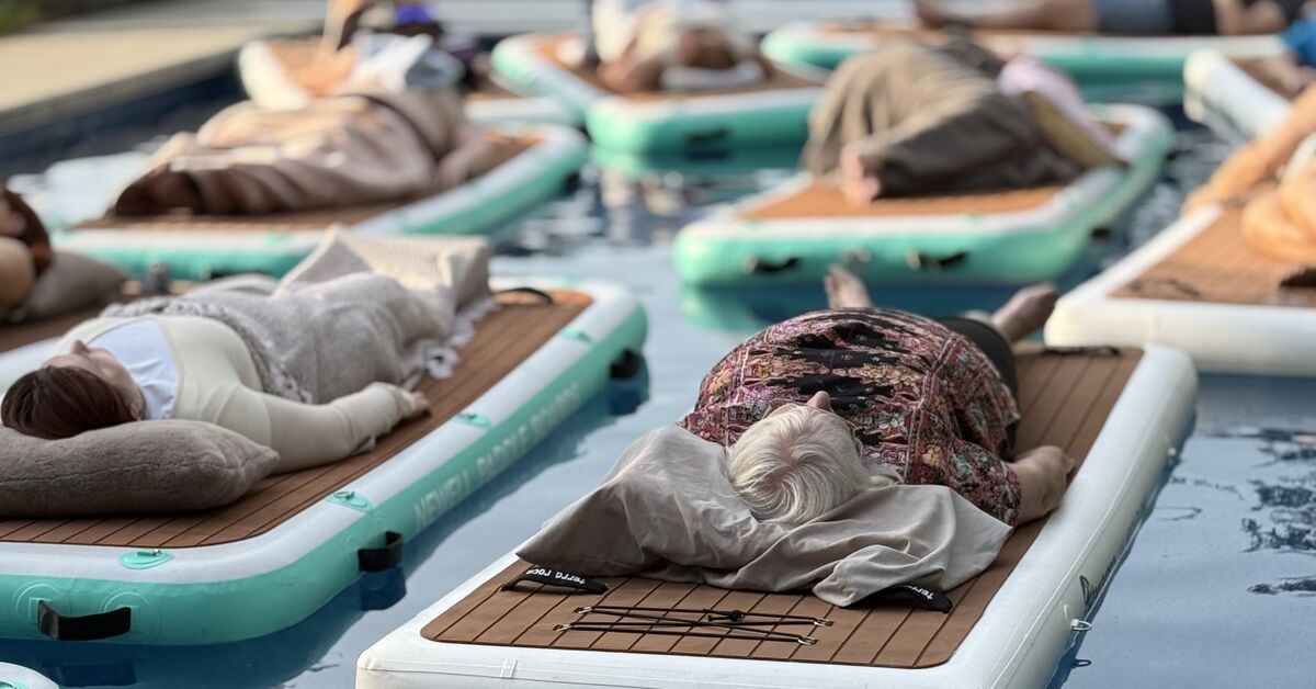 Guests lying on floating boards in a pool during a floating sound bath
