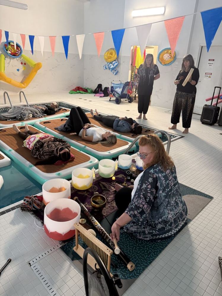 People lying on floating yoga mats in a pool, with musical instruments nearby.